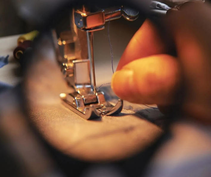 A person 's hand is seen through the lens of a sewing machine.